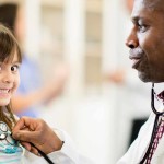 Physician using stethoscope on smiling girl